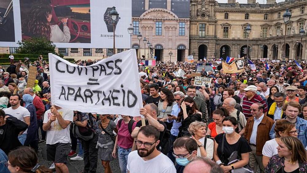 Protestujący przeciw szczepieniom trzymają transparent z napisem "Przepustka zdrowotna równa apartheidowi" podczas wiecu w Paryżu,